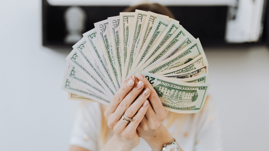 A person holding a fan of money in front of their face.