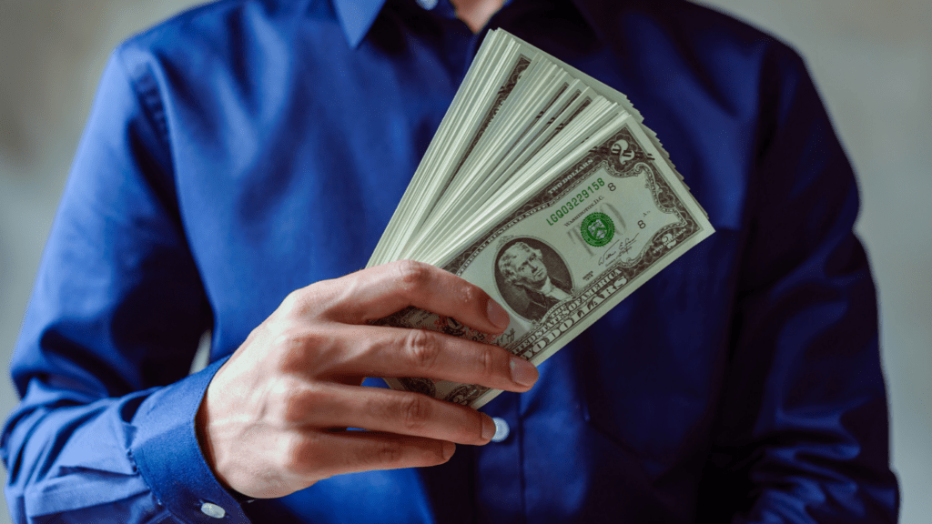A person holding a fan of money in front of their face.