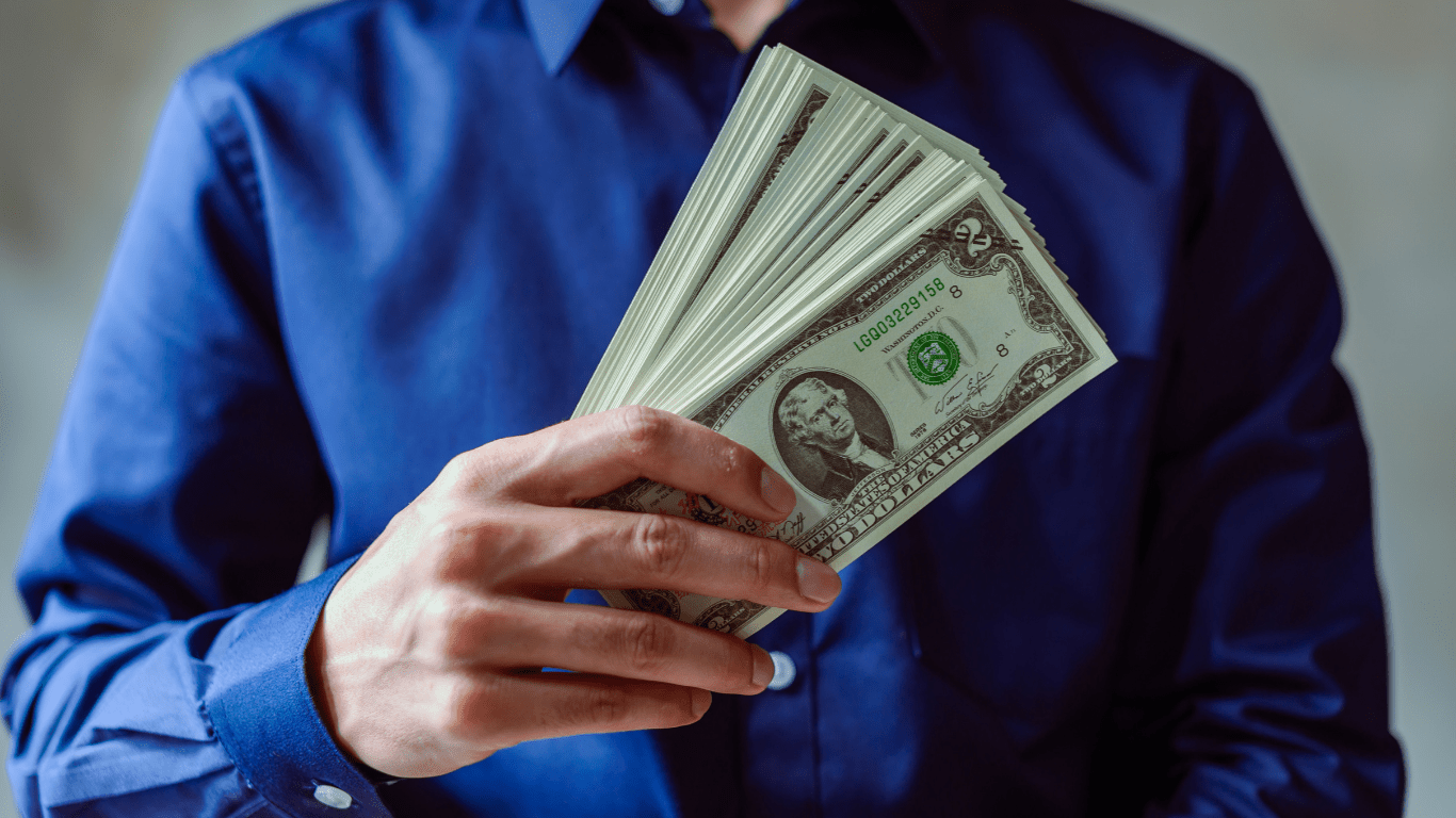 A person holding a fan of money in front of their face.